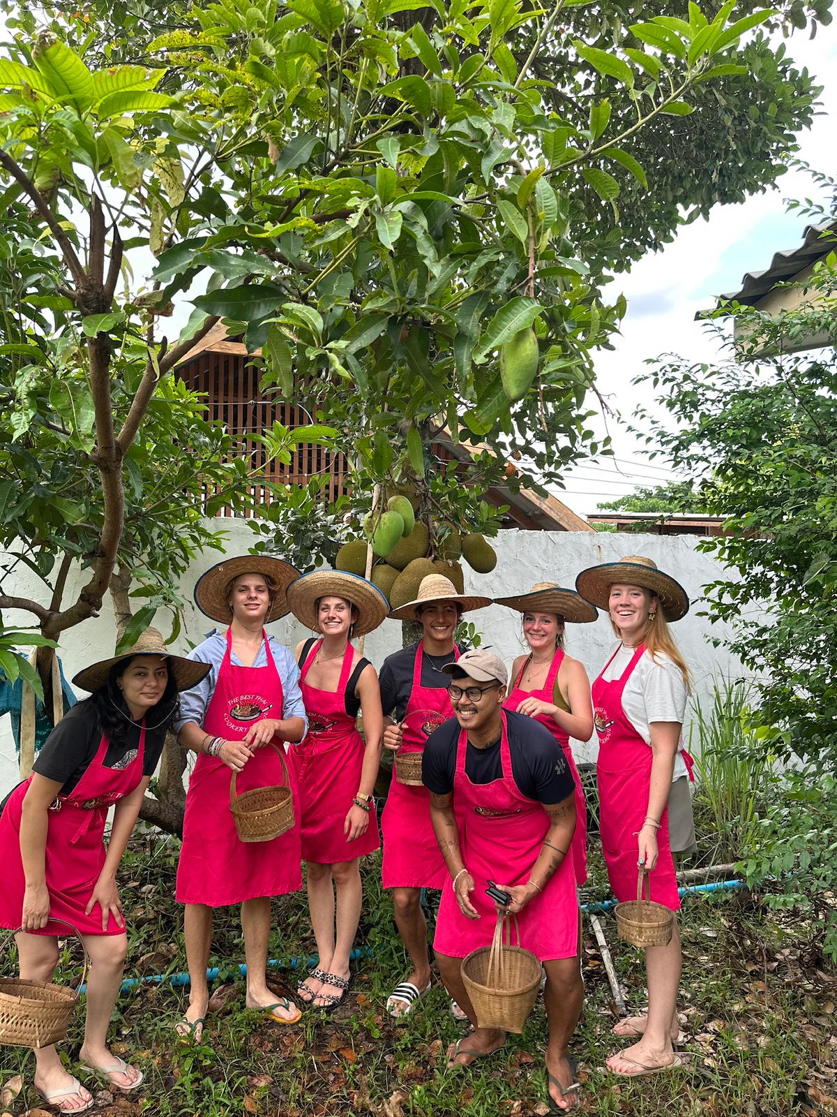 Group of students wearing pink aprons and straw hats posing together in the organic farm